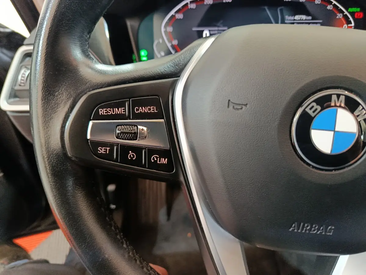 Gros plan sur le volant noir de la BMW Série 3 316d 2022, avec commandes de régulateur et logo central visible.