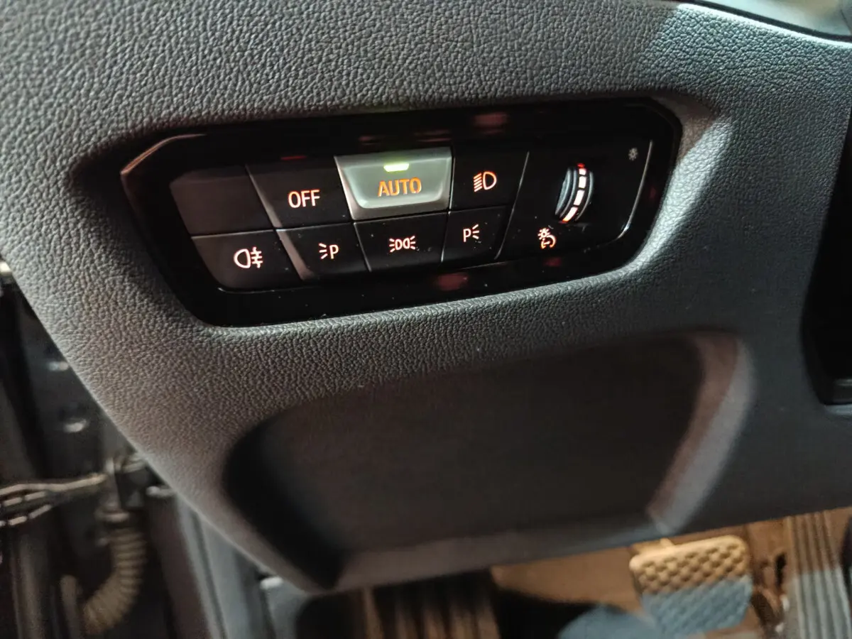 Gros plan sur les commandes d'éclairage à gauche du volant dans l'habitacle gris foncé d'une BMW Série 3 316d 2022.