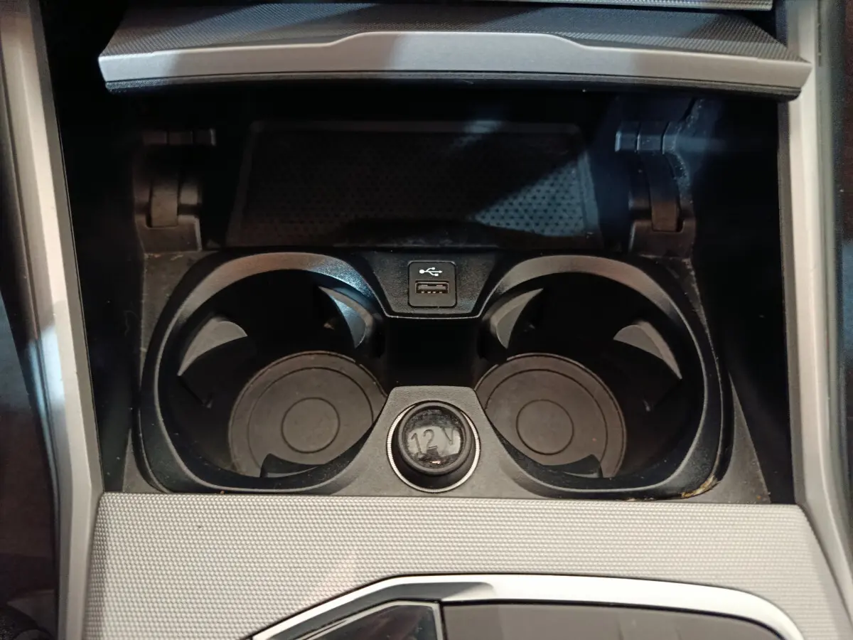 Gros plan sur les porte-gobelets noirs et prise 12V dans la console centrale d'une BMW Série 3 gris clair.