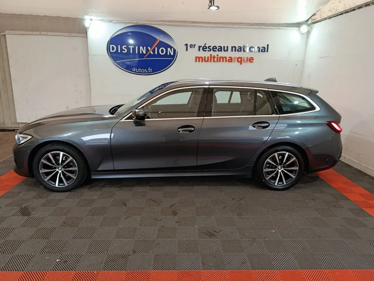 BMW Série 3 Touring gris clair vue de profil côté gauche en intérieur avec jantes alliage et feux arrière allumés