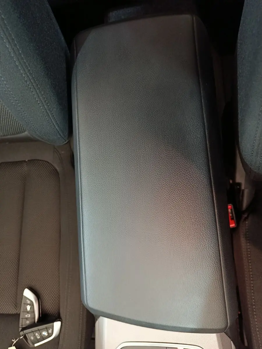 Vue plongeante sur l'accoudoir central noir et les sièges tissu gris foncé d'une BMW Série 3 316d 2022.