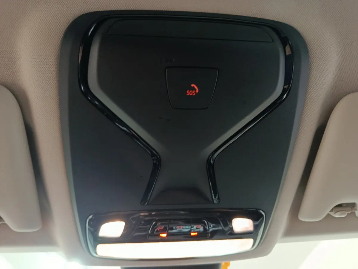Vue en gros plan du plafonnier noir avec bouton SOS rouge dans l'habitacle beige d'une BMW Série 3 gris clair 2022.