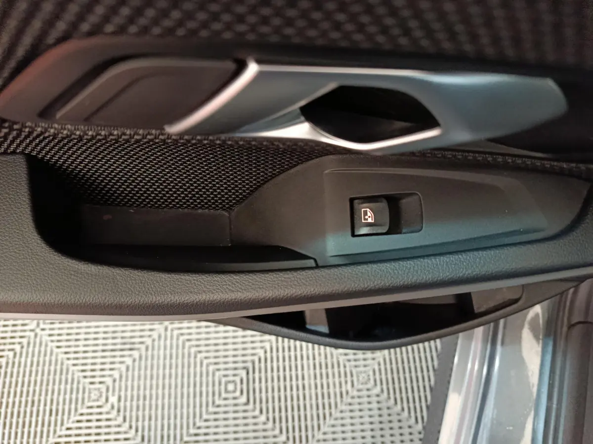 Gros plan sur la poignée intérieure et bouton de lève-vitre côté gauche d'une BMW Série 3 gris clair 2022.