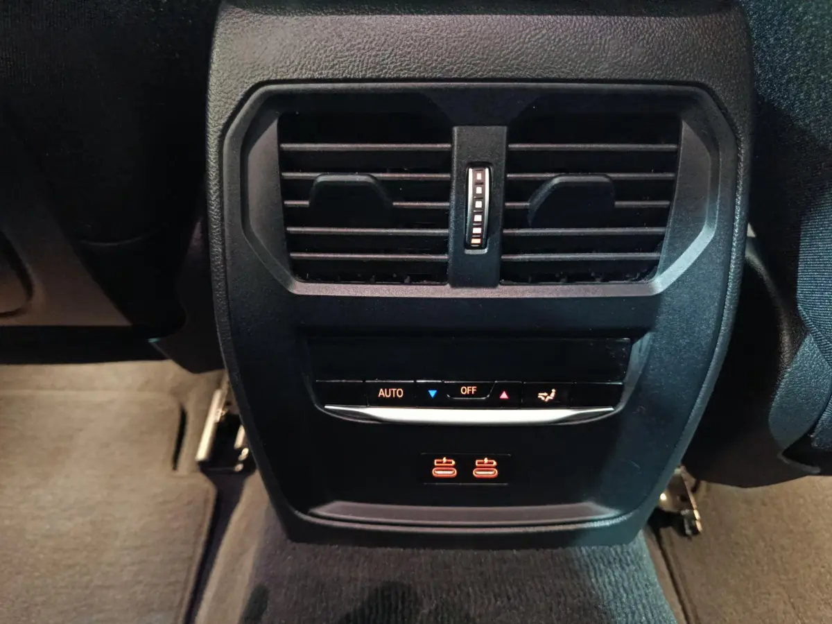 Vue rapprochée des commandes de climatisation arrière et prises USB illuminées dans une BMW Série 3 gris clair 2022.