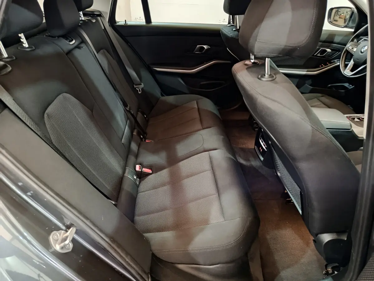 Vue intérieure côté gauche sur la banquette arrière noire et l'avant du tableau de bord d'une BMW Série 3 gris clair 2022.