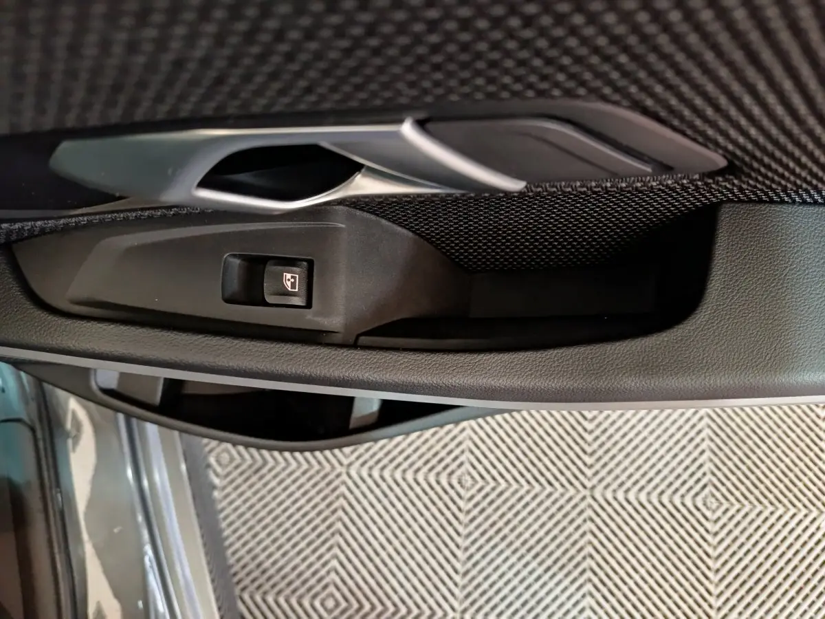 Poignée intérieure côté gauche gris foncé avec bouton de commande de vitre sur BMW Série 3 316d 2022 gris clair.