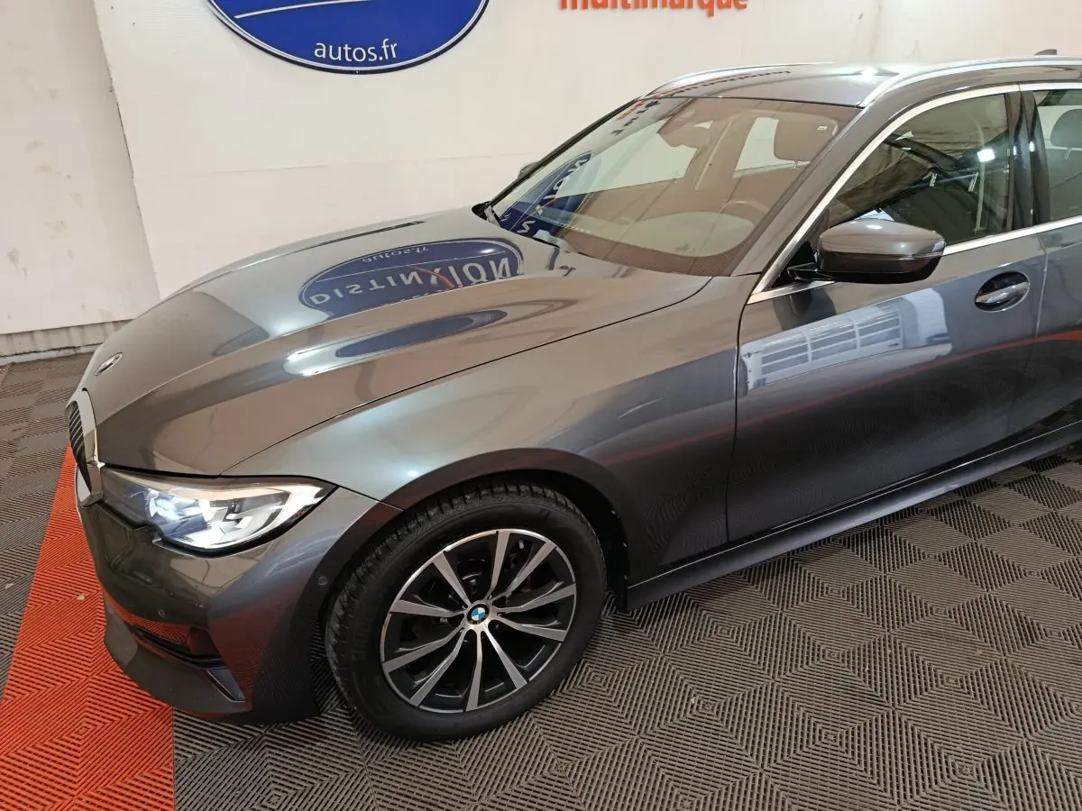 Vue 3/4 avant droit d'une BMW Série 3 gris clair avec phares LED allumés et jantes alliage noires.