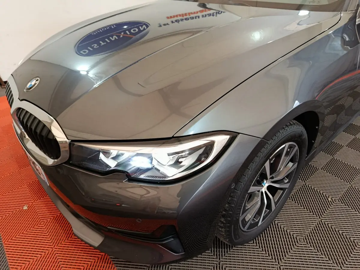 Vue 3/4 avant droit d'une BMW Série 3 gris clair avec phares LED allumés et jantes alliage distinctives.