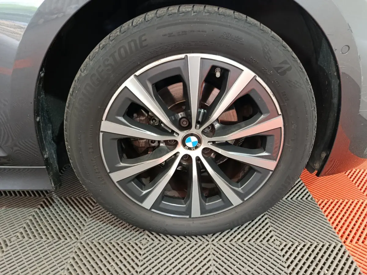 Gros plan sur la roue avant gauche gris clair d'une BMW Série 3 316d avec jante alliage et logo BMW au centre.