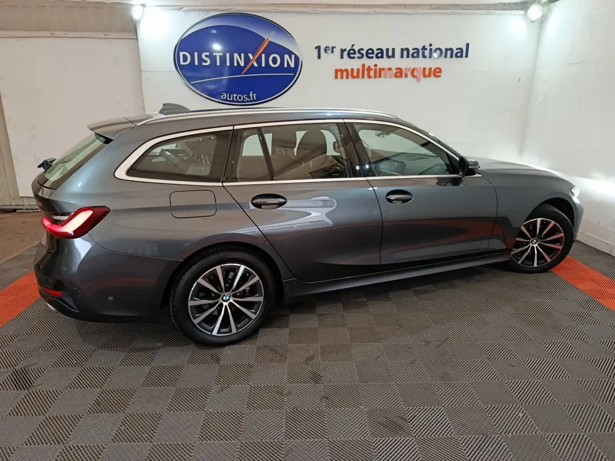 BMW Série 3 316d gris clair vue de profil côté droit, avec feux arrière allumés et jantes alliage distinctives.