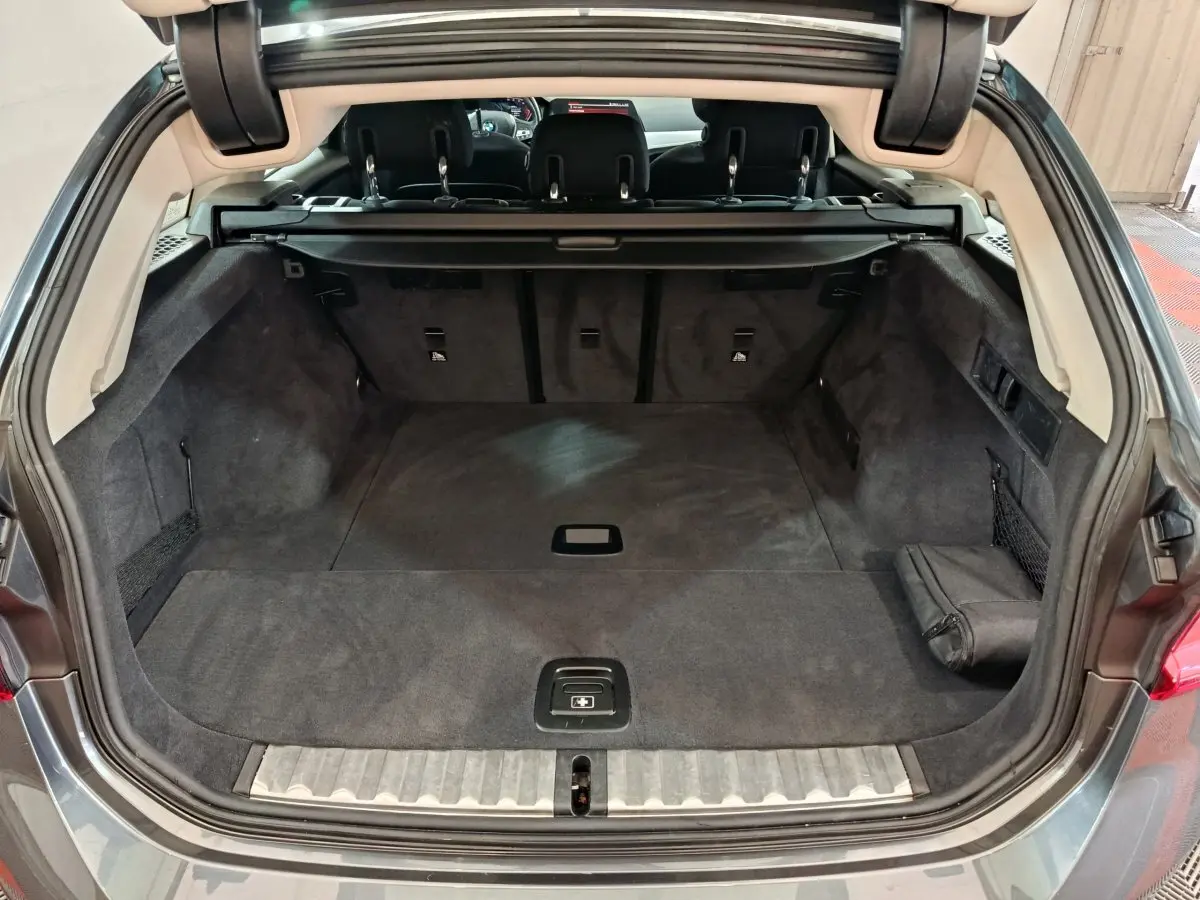 Coffre spacieux ouvert de la BMW Série 3 316d gris clair, vue arrière avec banquette et cache-bagages visibles.