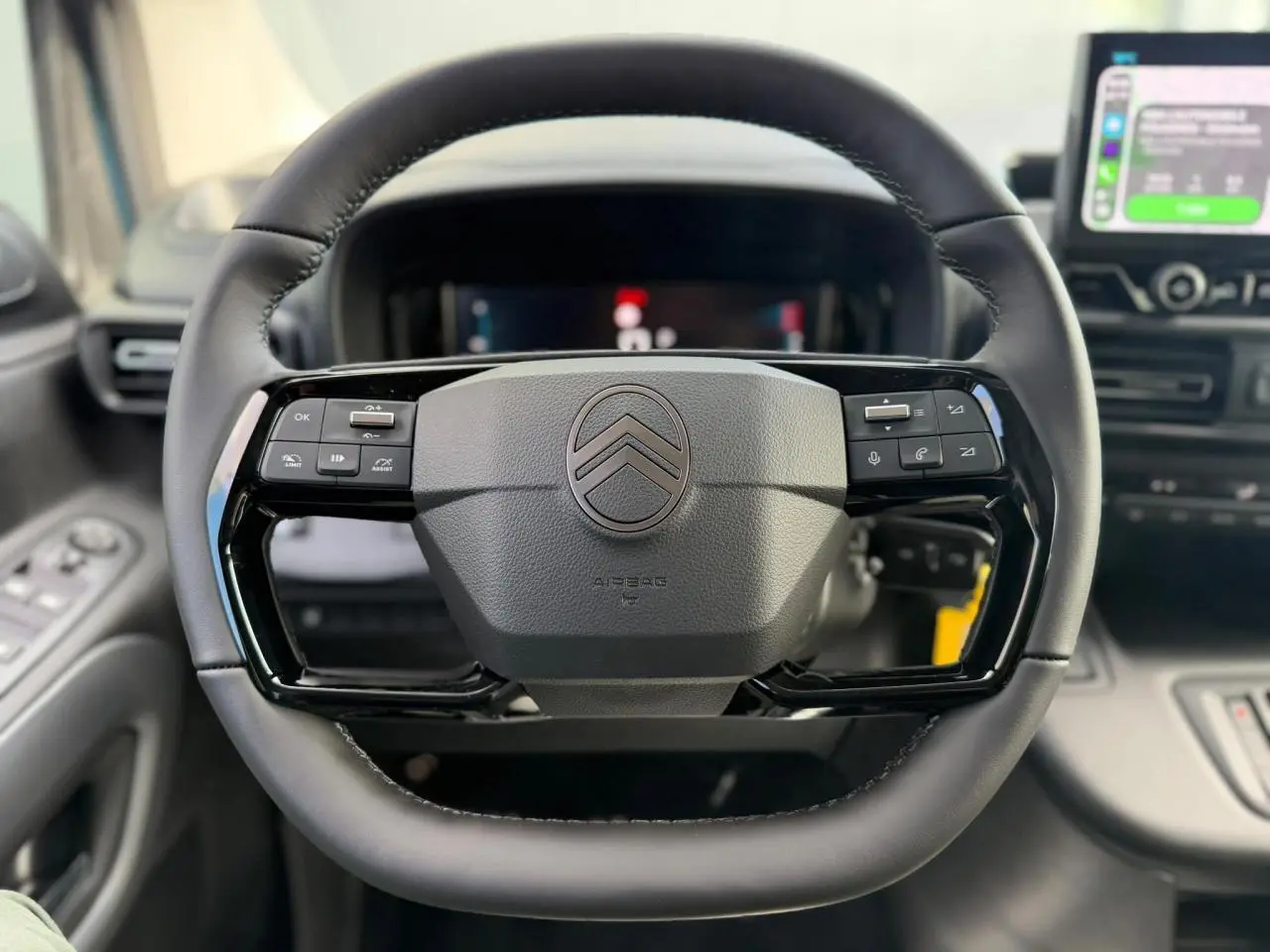 Vue rapprochée du volant cuir multifonctions noir du Citroën Berlingo Multispace 2026, avec tableau de bord numérique en arrière-plan.