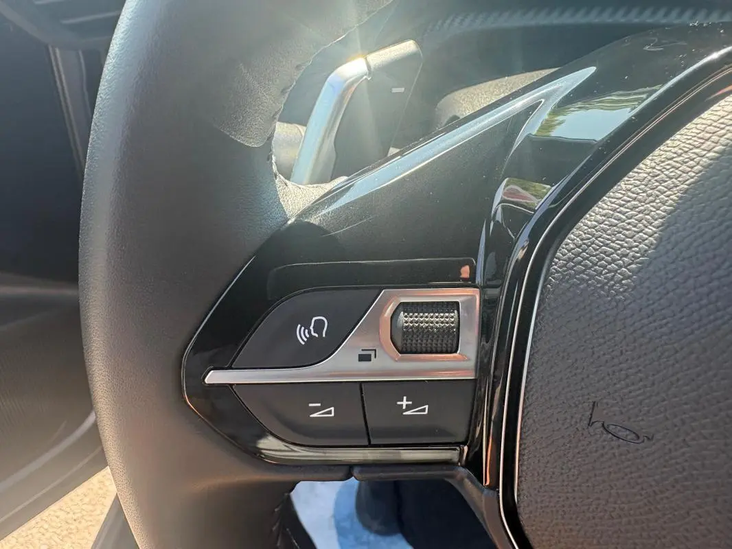 Gros plan sur les commandes gauche du volant noir du Peugeot 2008 Hybrid 145 gris, avec molette et boutons de volume.