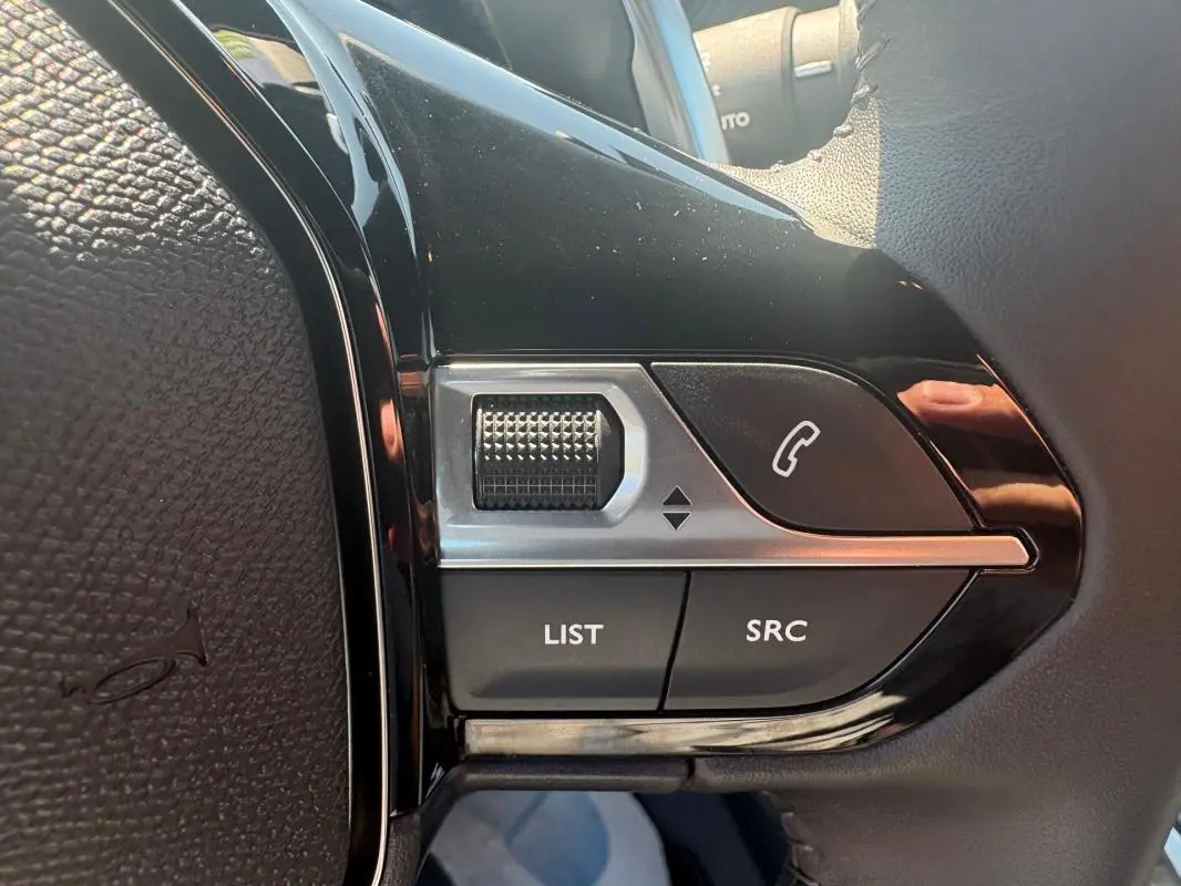 Gros plan sur les commandes multimédia au volant du Peugeot 2008 Hybrid 145 gris, avec molette et boutons d’appel.