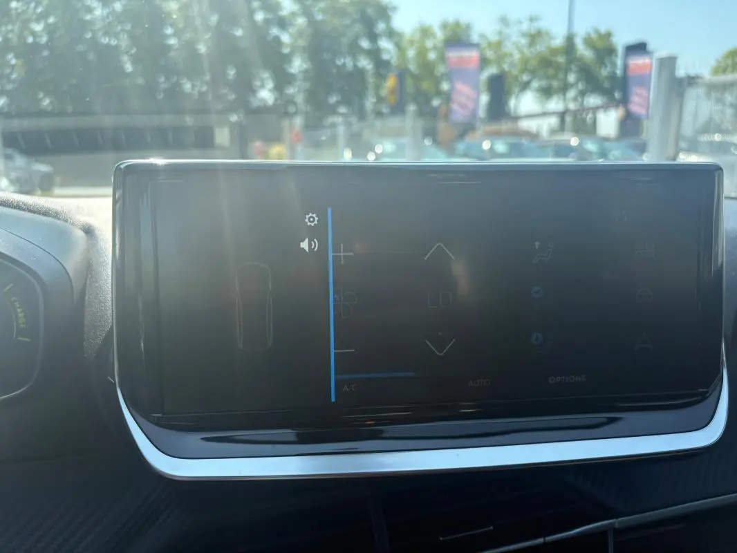 Écran tactile du tableau de bord du Peugeot 2008 Hybrid 145 gris, vue frontale intérieure avec reflet extérieur.