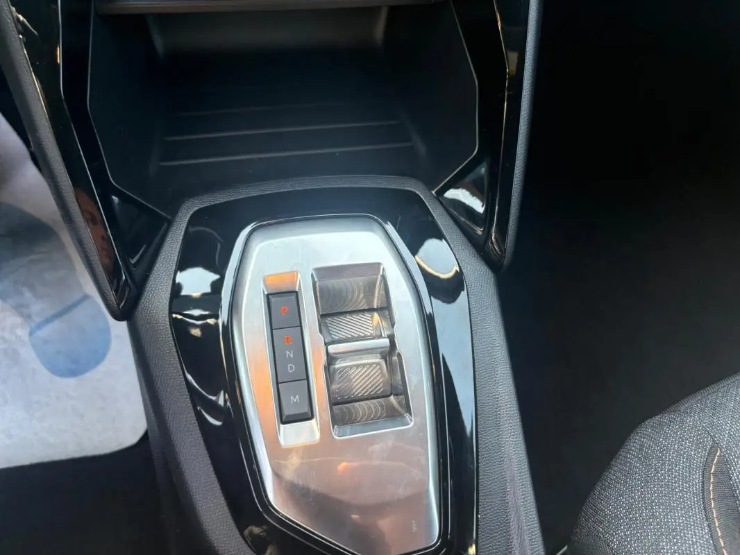 Gros plan sur la console centrale du Peugeot 2008 Hybrid 145 gris, montrant la commande de boîte automatique et les commandes de réglage.