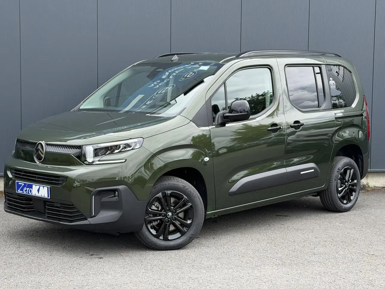 Vue 3/4 avant droite d'un Citroën Berlingo Multispace vert Sirkka avec jantes noires et barres de toit noires.