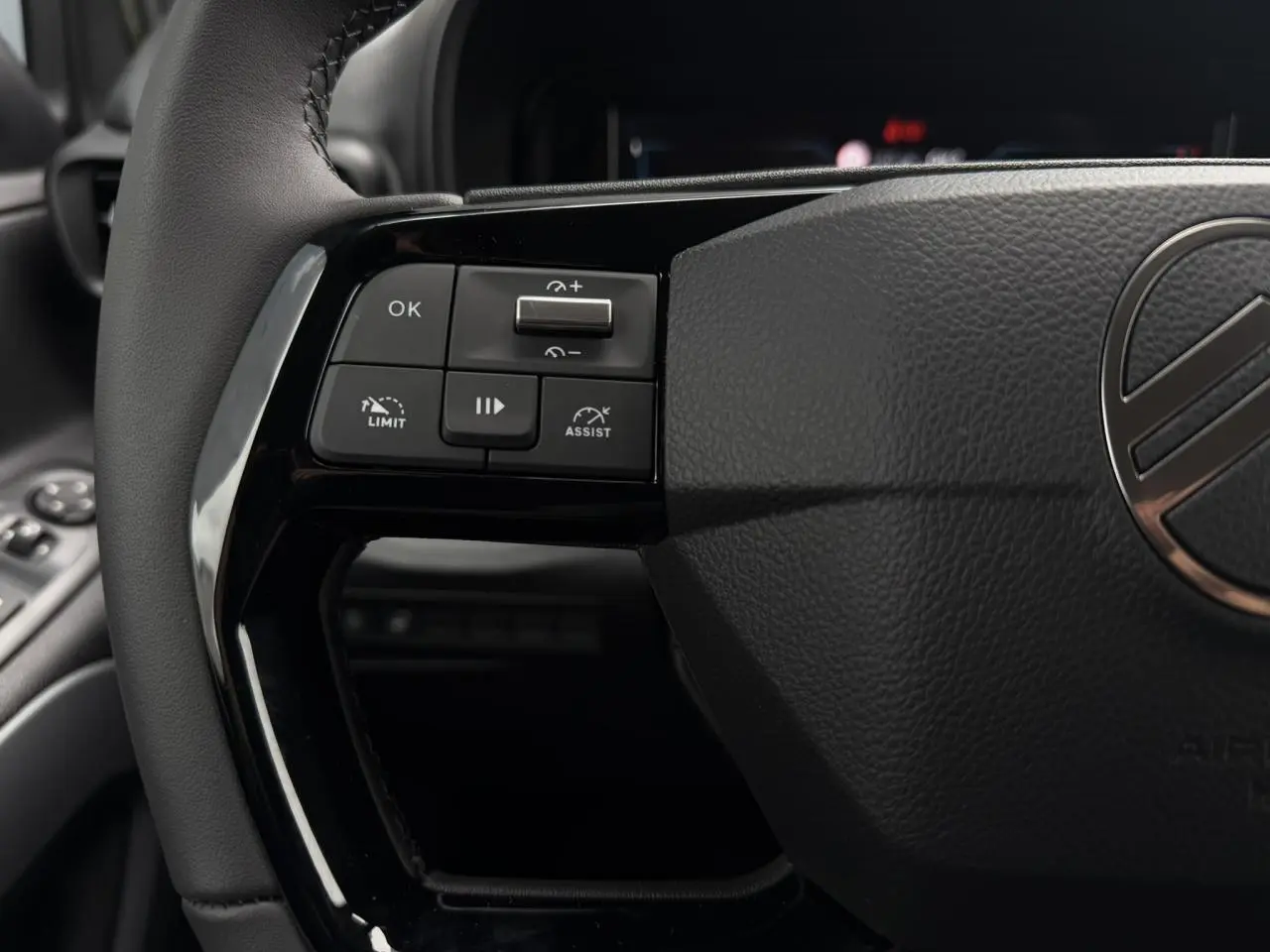Gros plan sur les commandes gauche du volant cuir noir du Citroën Berlingo Multispace 2026, intérieur sombre.
