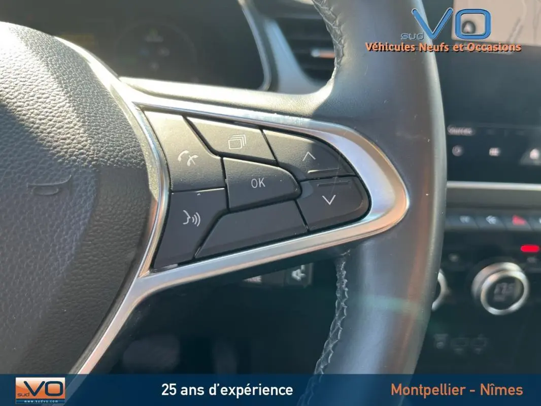 Gros plan sur les commandes au volant cuir du Renault Captur rouge E-Tech Plug-in 160 Intens, tableau de bord en arrière-plan flou.