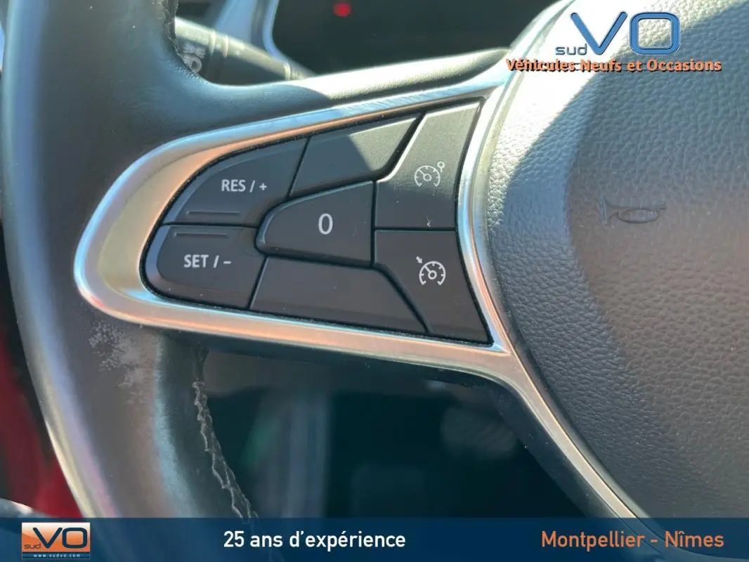 Gros plan sur les commandes du régulateur de vitesse au volant cuir du Renault Captur E-Tech rouge de 2020.