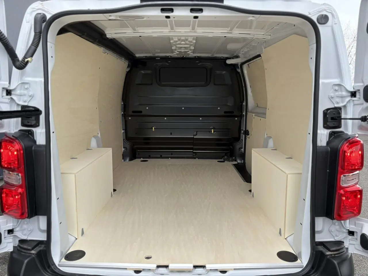 Vue arrière du fourgon Peugeot Expert blanc Icy, montrant l'espace de chargement vide avec habillage bois clair.