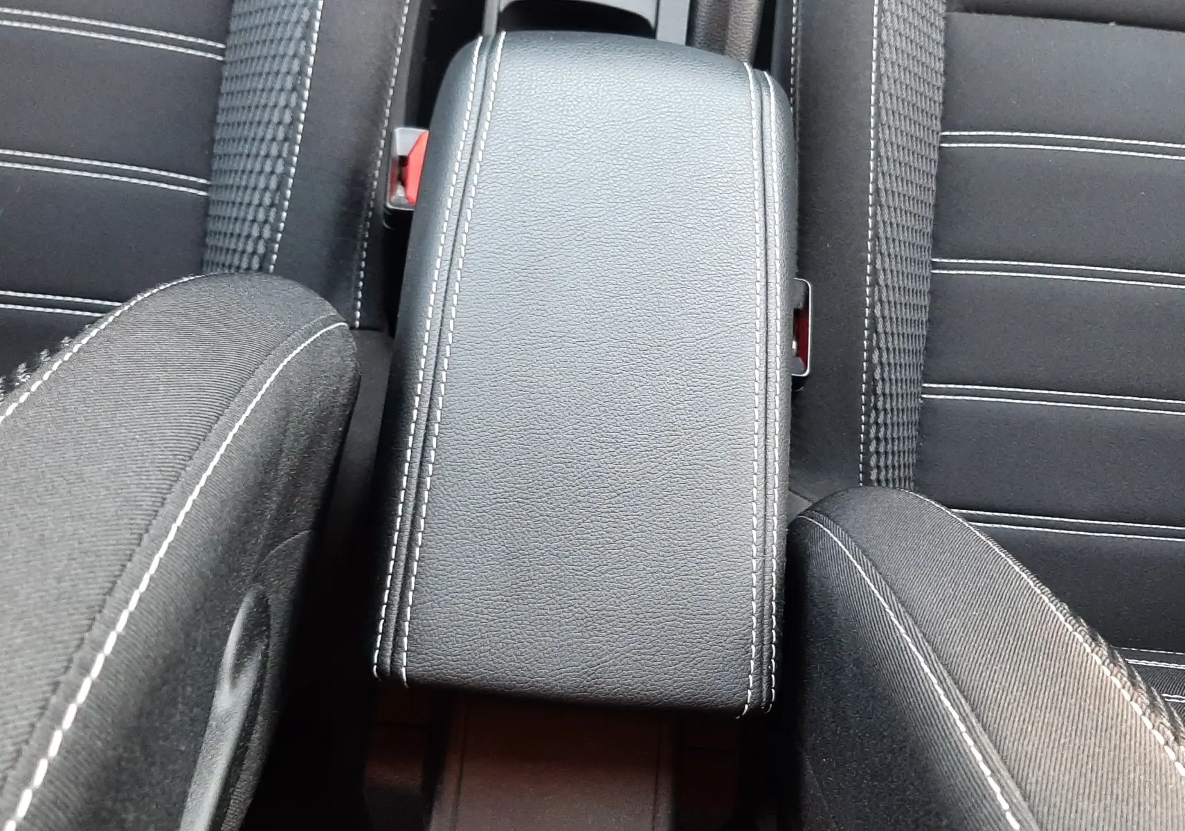 Vue plongeante sur l'accoudoir central noir avec surpiqûres blanches entre les sièges avant du Dacia Duster 2023.