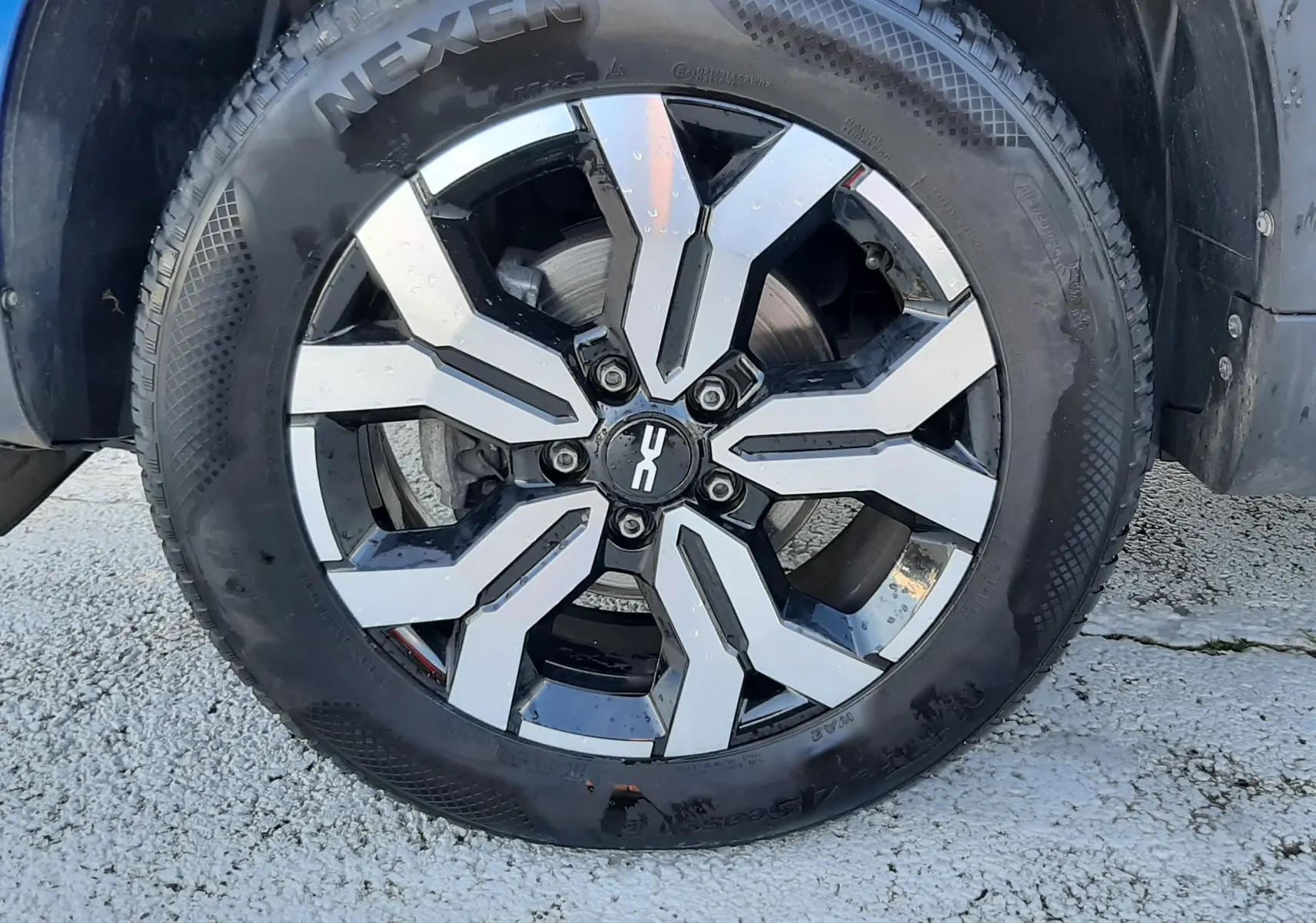 Vue rapprochée de l'arrière droit d'un Dacia Duster bleu 2023, montrant la roue et l'aile avec protection noire.