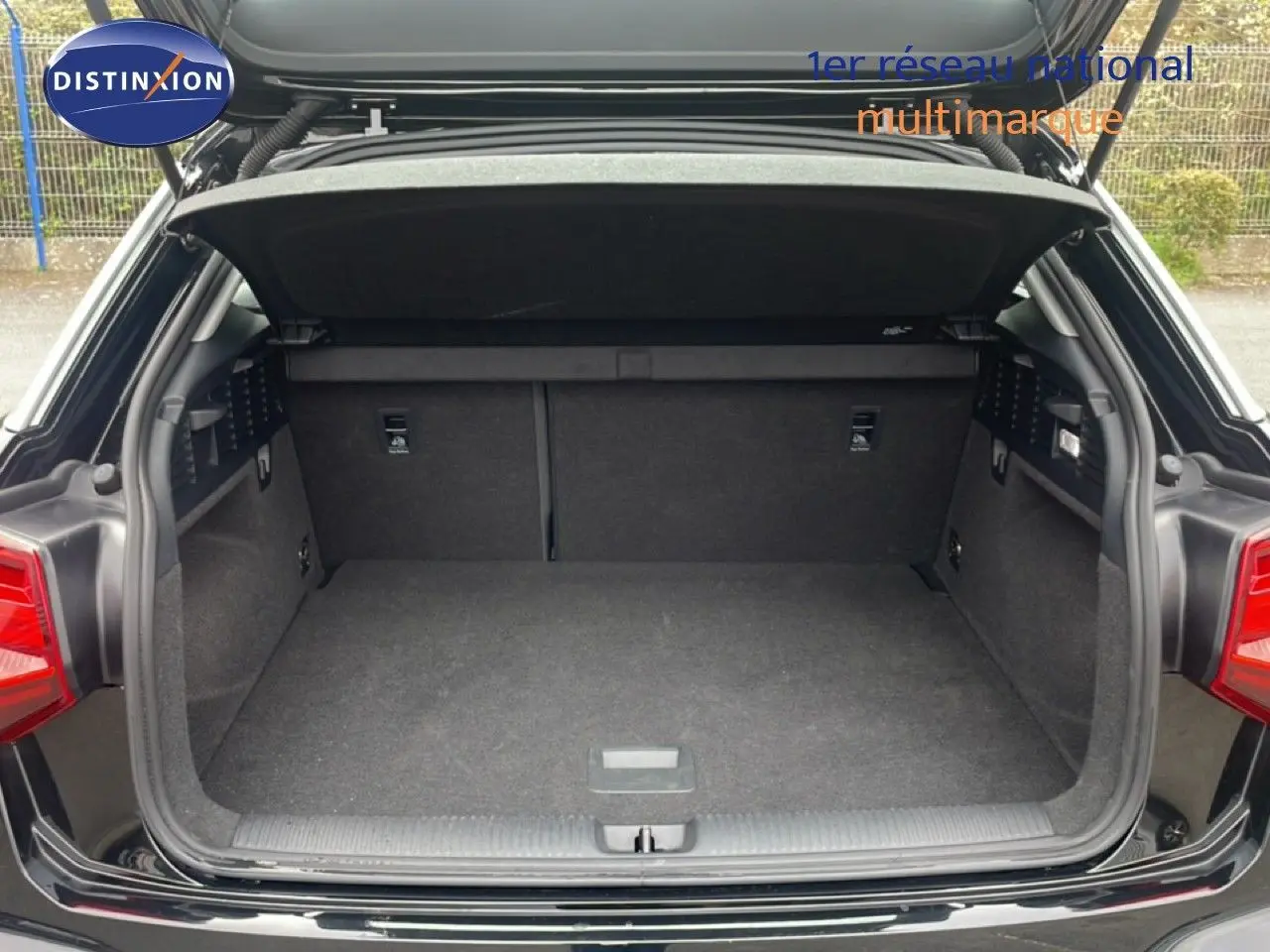 Coffre ouvert vu de l'arrière d'un Audi Q2 noir mito metal, montrant l'espace de chargement vide et les garnitures intérieures.
