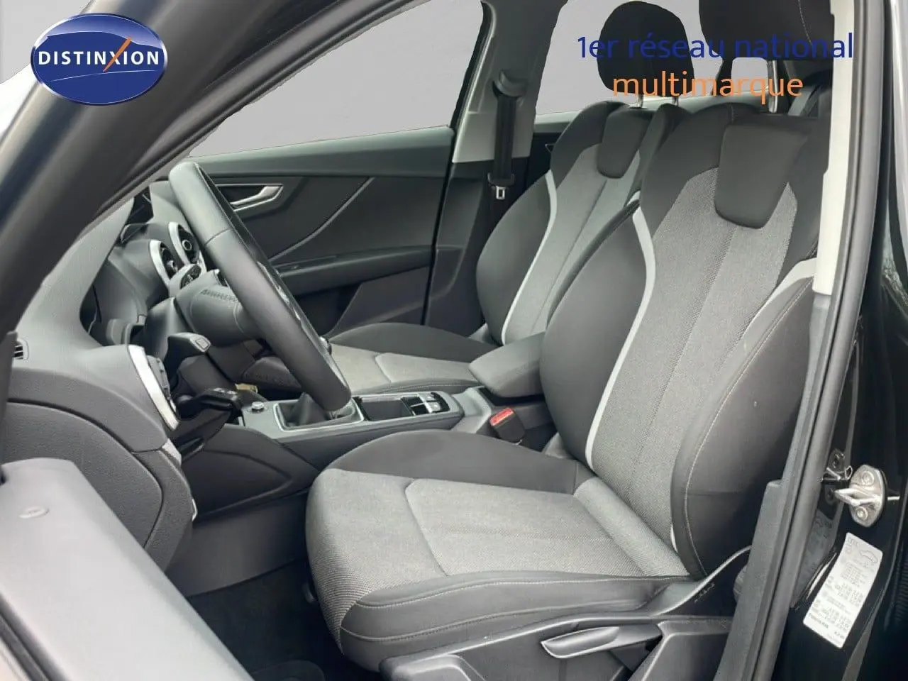 Vue intérieure côté conducteur de l'Audi Q2 30 TDI S-Line 2025 avec sièges tissu gris et noir et volant multifonction.
