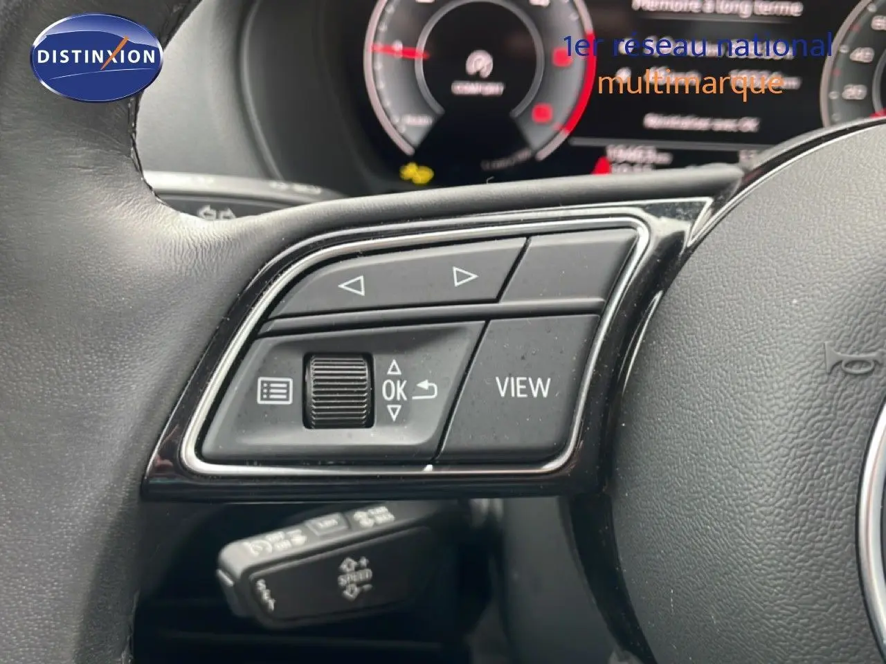 Gros plan sur les commandes au volant noir de l'Audi Q2 30 TDI S-Line 2025 avec tableau de bord numérique en arrière-plan flou.