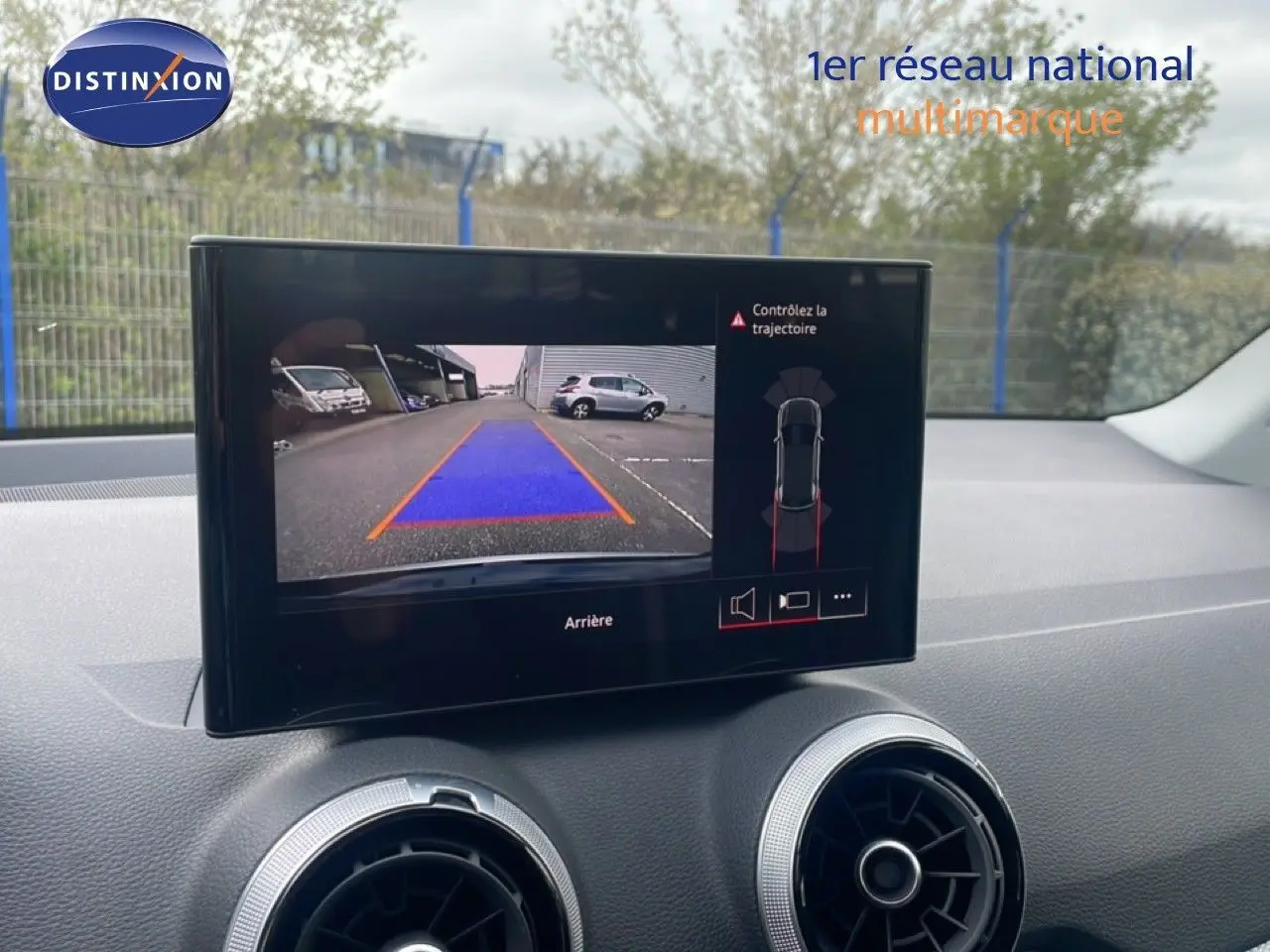 Écran central affichant la caméra de recul d’un Audi Q2 noir mito metal, avec guidage de trajectoire en bleu et orange.