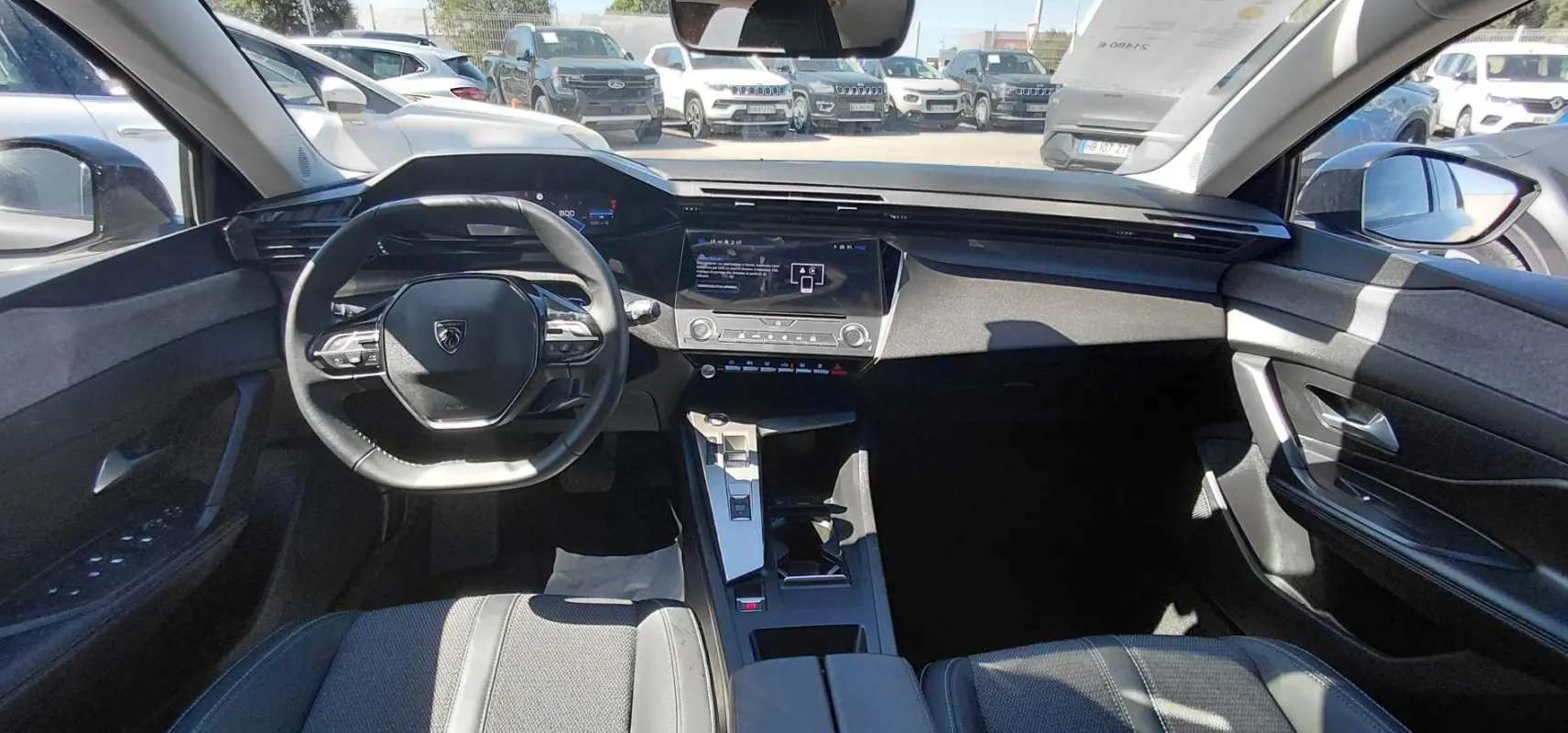 Vue intérieure avant de la Peugeot 308 gris, montrant le volant compact, le cockpit numérique et la console centrale moderne.