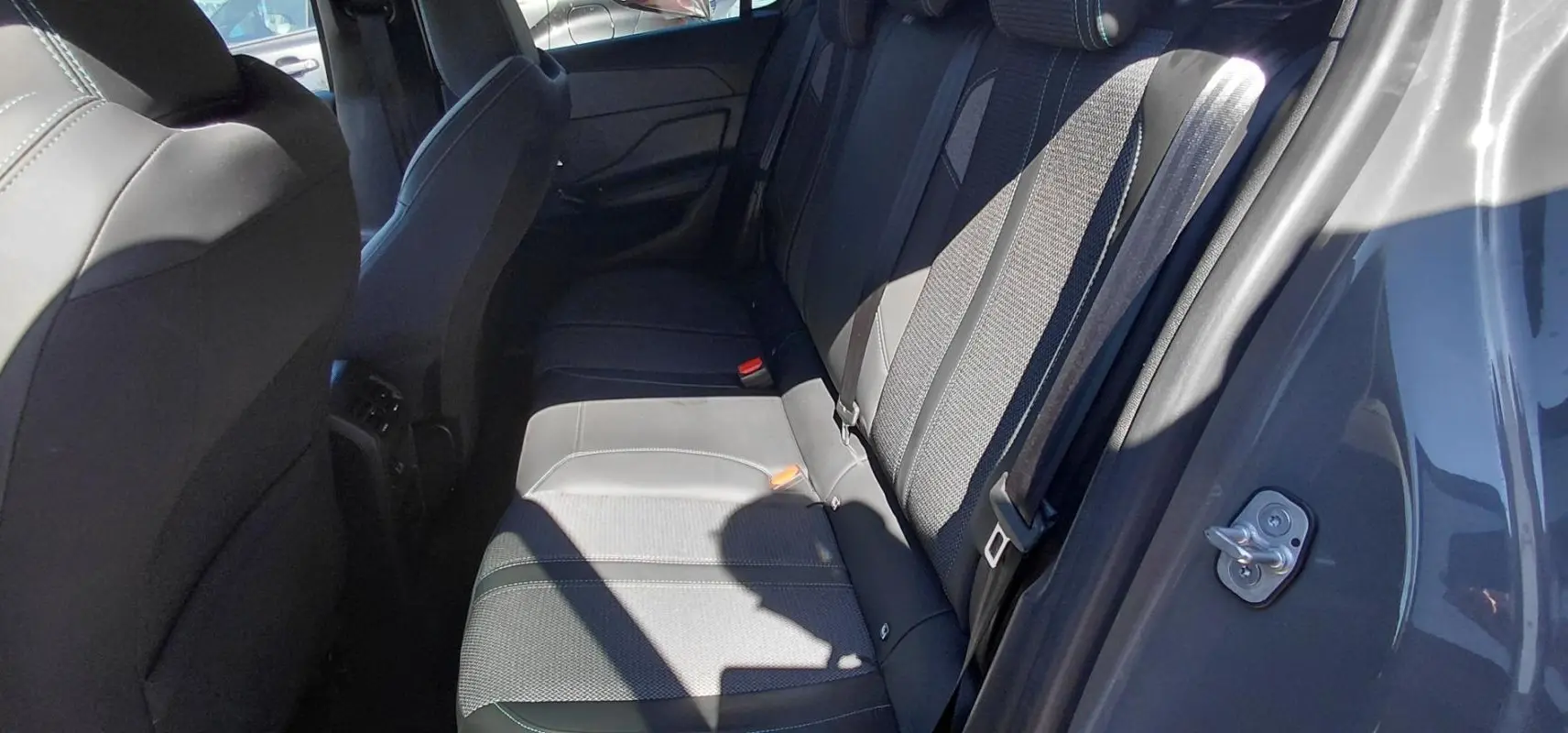 Vue intérieure des sièges arrière gris d'une Peugeot 308 2025, avec ceinture de sécurité et porte ouverte côté droit.