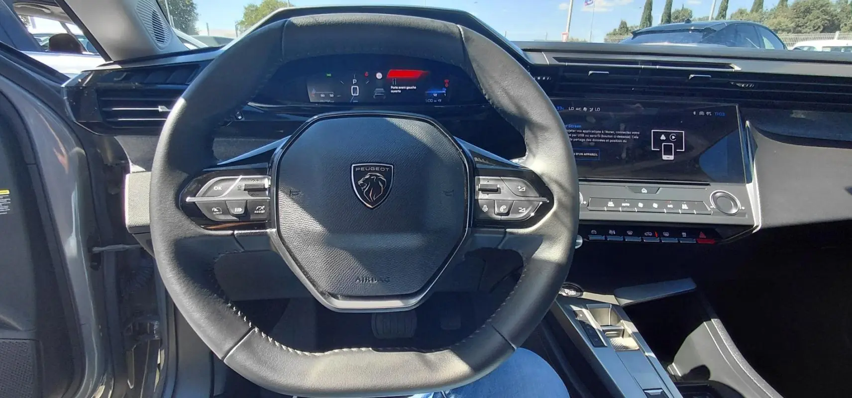 Vue intérieure centrée sur le volant cuir noir et le cockpit numérique de la Peugeot 308 gris 2025.