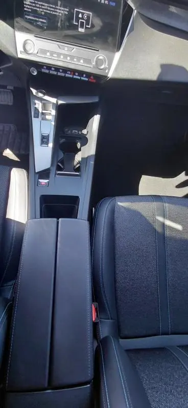 Vue plongeante sur la console centrale noire et l'accoudoir du Peugeot 308 gris, avec levier de boîte automatique et sièges en tissu.