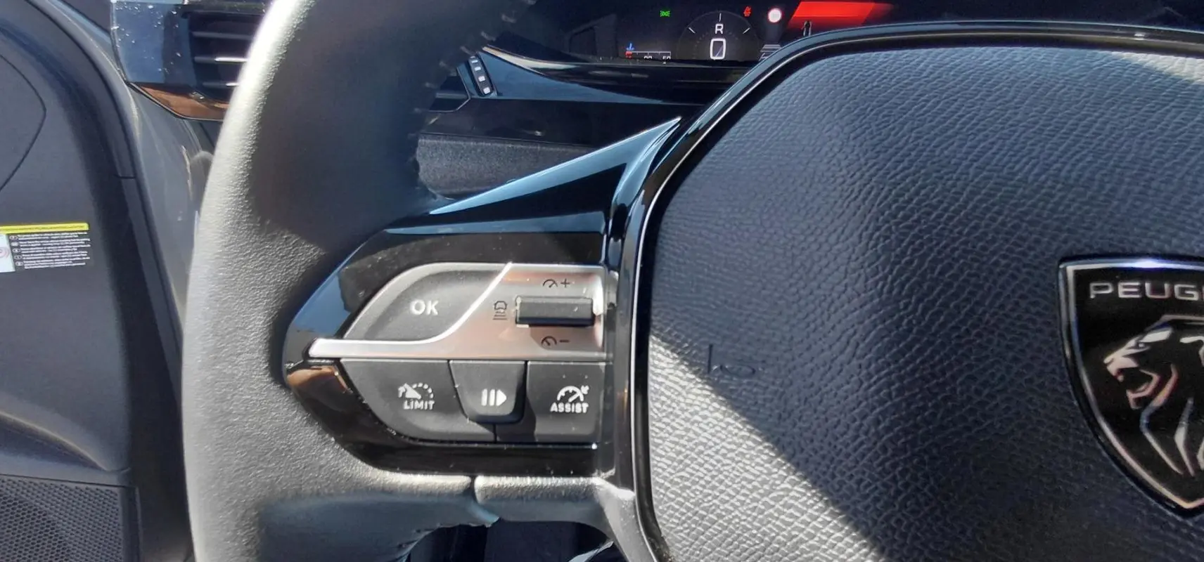Gros plan sur le volant gris du Peugeot 308 2025, avec commandes intégrées et logo lion visible.