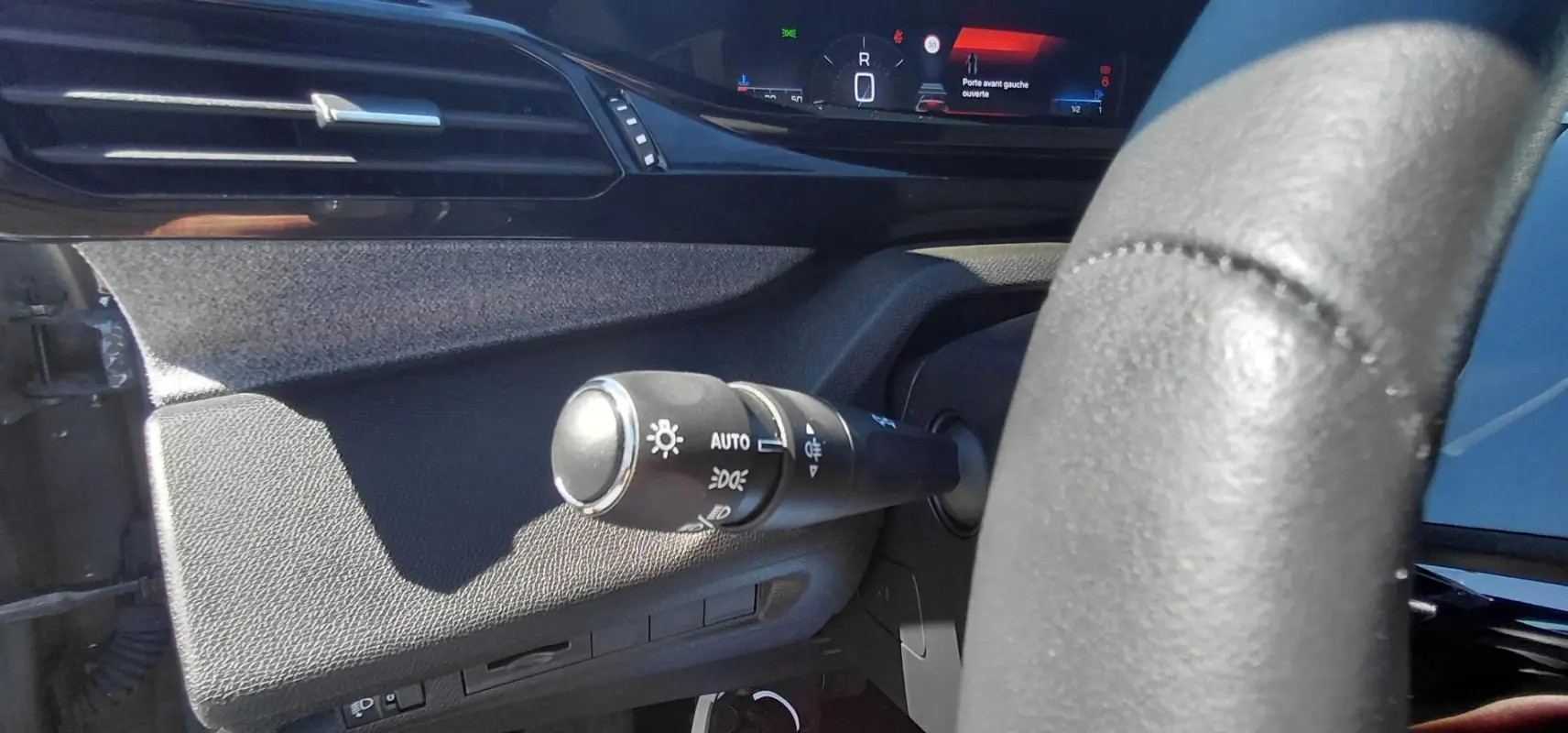 Gros plan sur la commande des feux à gauche du volant dans l’habitacle gris du Peugeot 308 2025, affichage numérique visible.