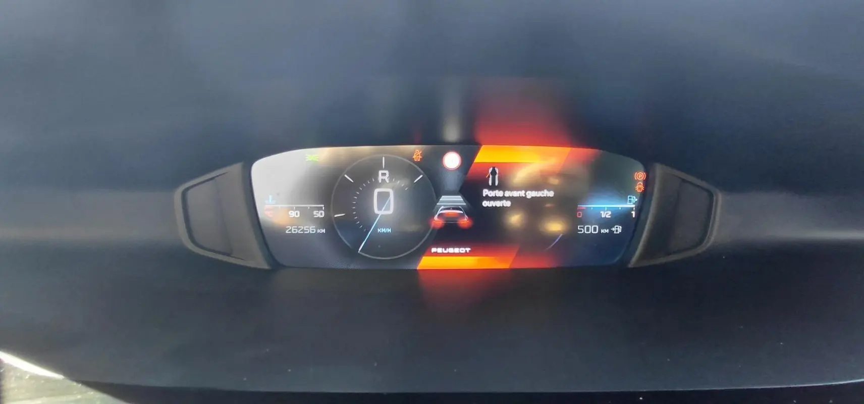 Vue rapprochée du cockpit numérique de la Peugeot 308 gris, affichant la vitesse, l'alerte porte avant gauche ouverte et l'autonomie.
