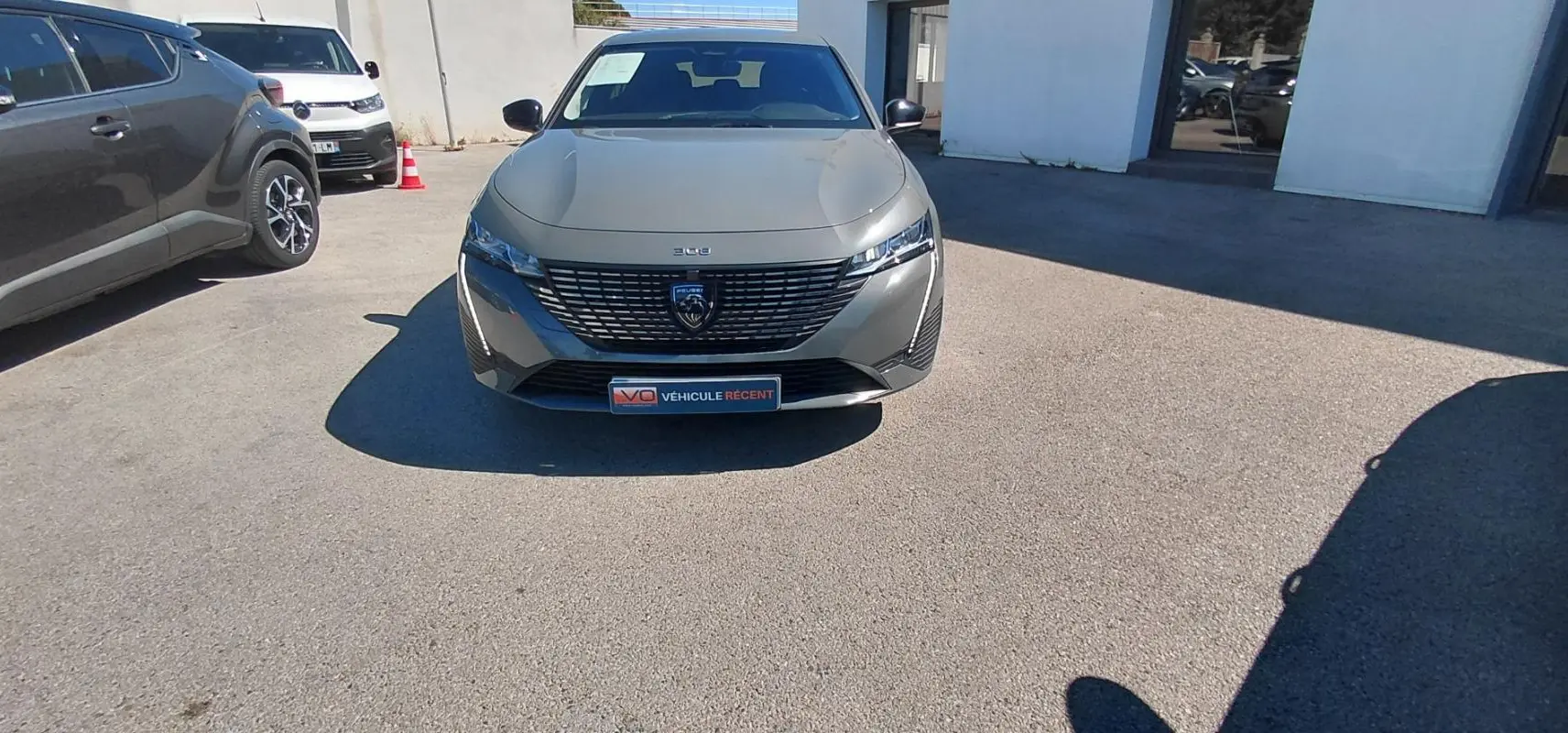 Vue de face d'une Peugeot 308 gris métallisé 2025 avec calandre distinctive et phares fins, stationnée en extérieur.