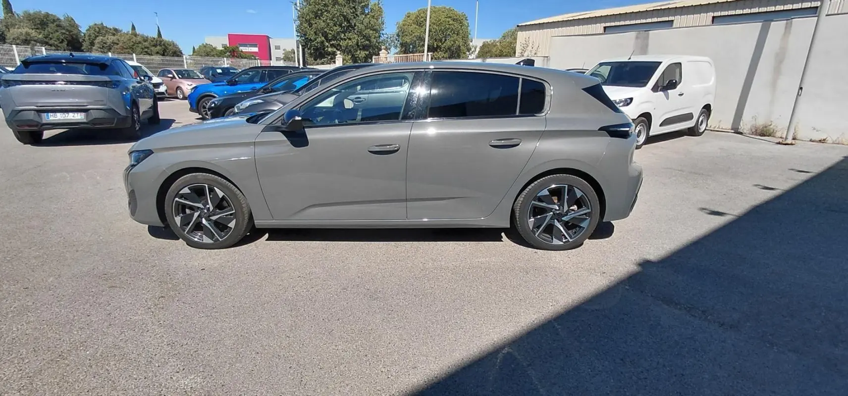 Vue de profil côté gauche d'une Peugeot 308 gris métallisé garée en extérieur sur un parking.