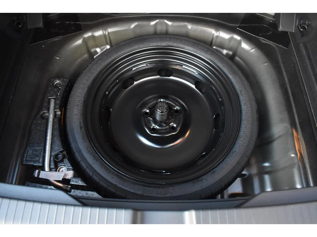Vue plongeante sur la roue de secours noire à encombrement réduit dans le coffre d’un Volkswagen T-Roc Grenadilla Black.