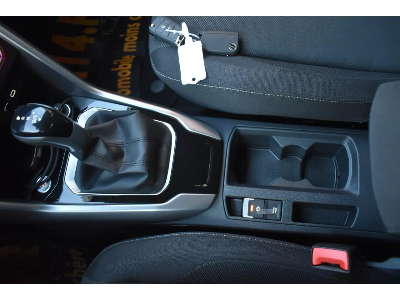Vue intérieure en plongée sur la console centrale du Volkswagen T-Roc noir, avec levier de boîte automatique et porte-gobelets.