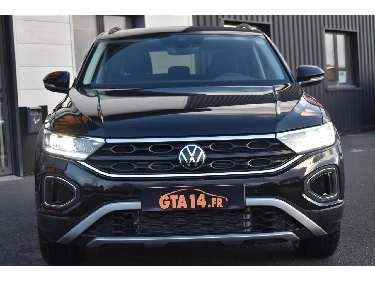 Vue de face du Volkswagen T-Roc 2025 noir Grenadilla avec calandre hexagonale et feux LED allumés.