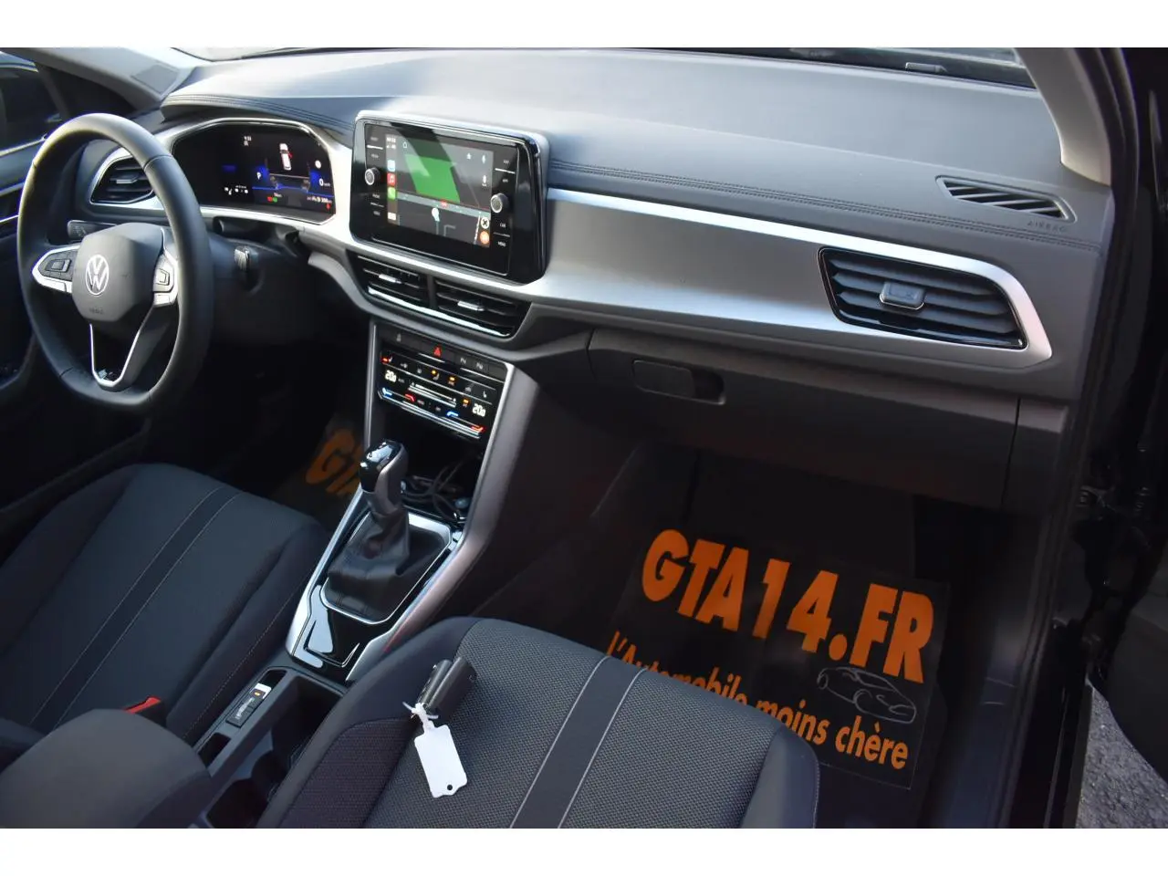 Vue intérieure côté passager avant du Volkswagen T-Roc 2025, sellerie tissu noir et console centrale avec écran tactile.