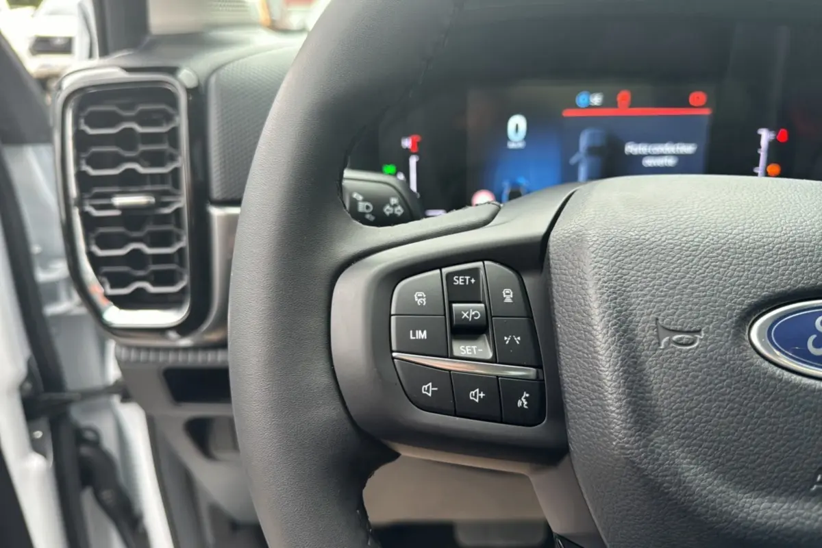 Gros plan sur le volant multifonctions noir du Ford Ranger 2025 avec commandes au volant et tableau de bord numérique flou.