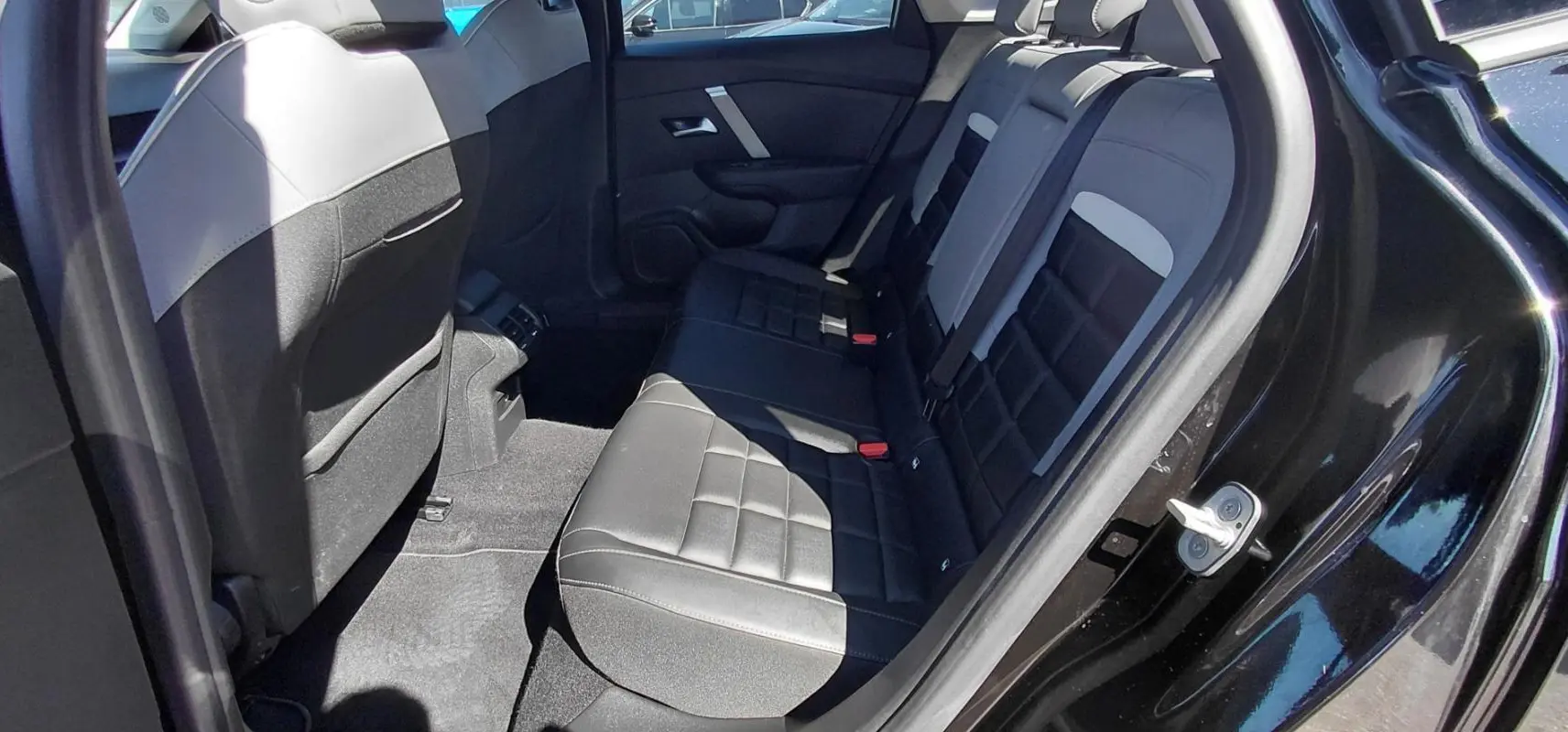 Vue intérieure côté droit des sièges arrière en cuir noir et gris d'une Citroën C4 X hybride 2025 avec accoudoir central.