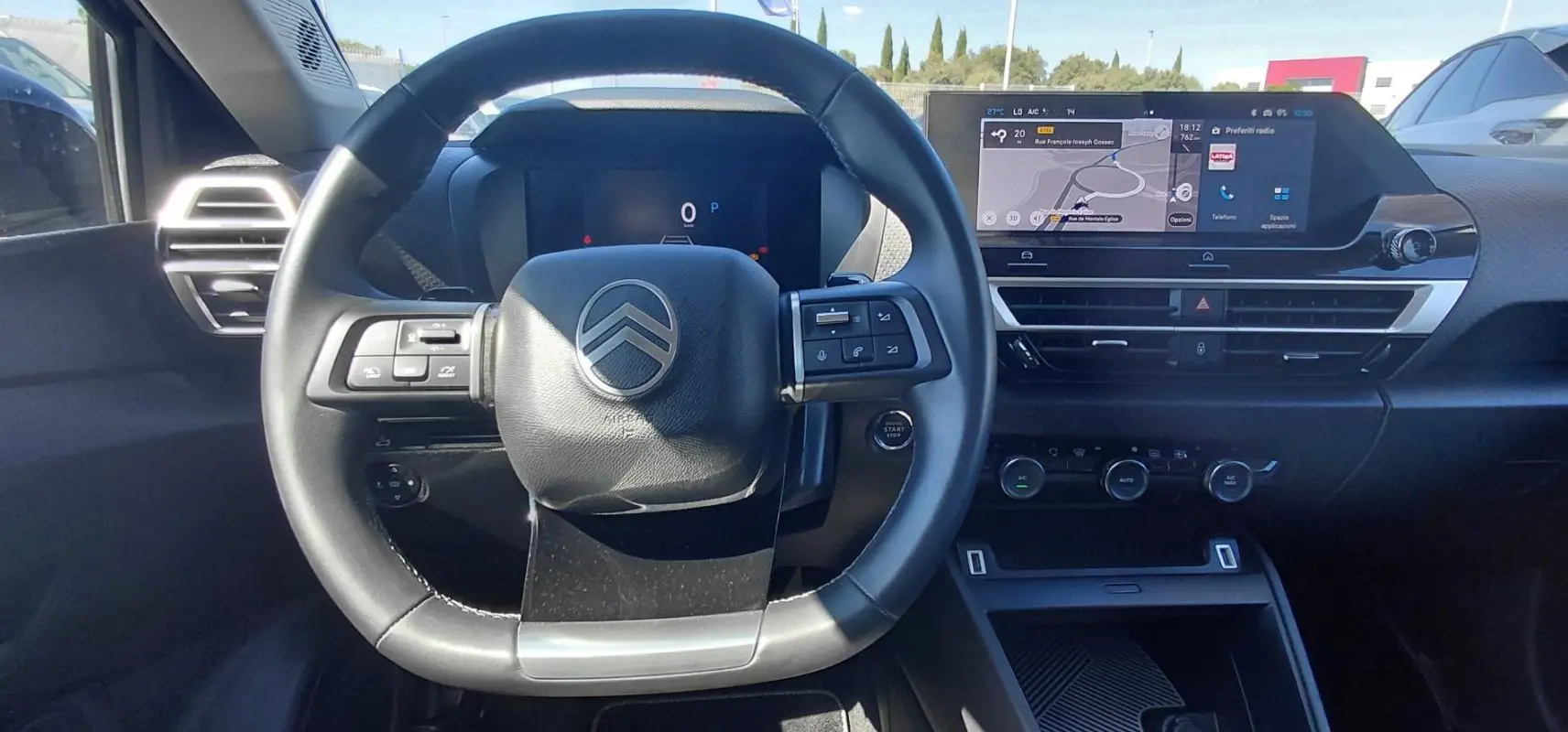Vue intérieure centrée sur le volant cuir et le tableau de bord numérique du Citroën C4 X noir 2025 hybride.