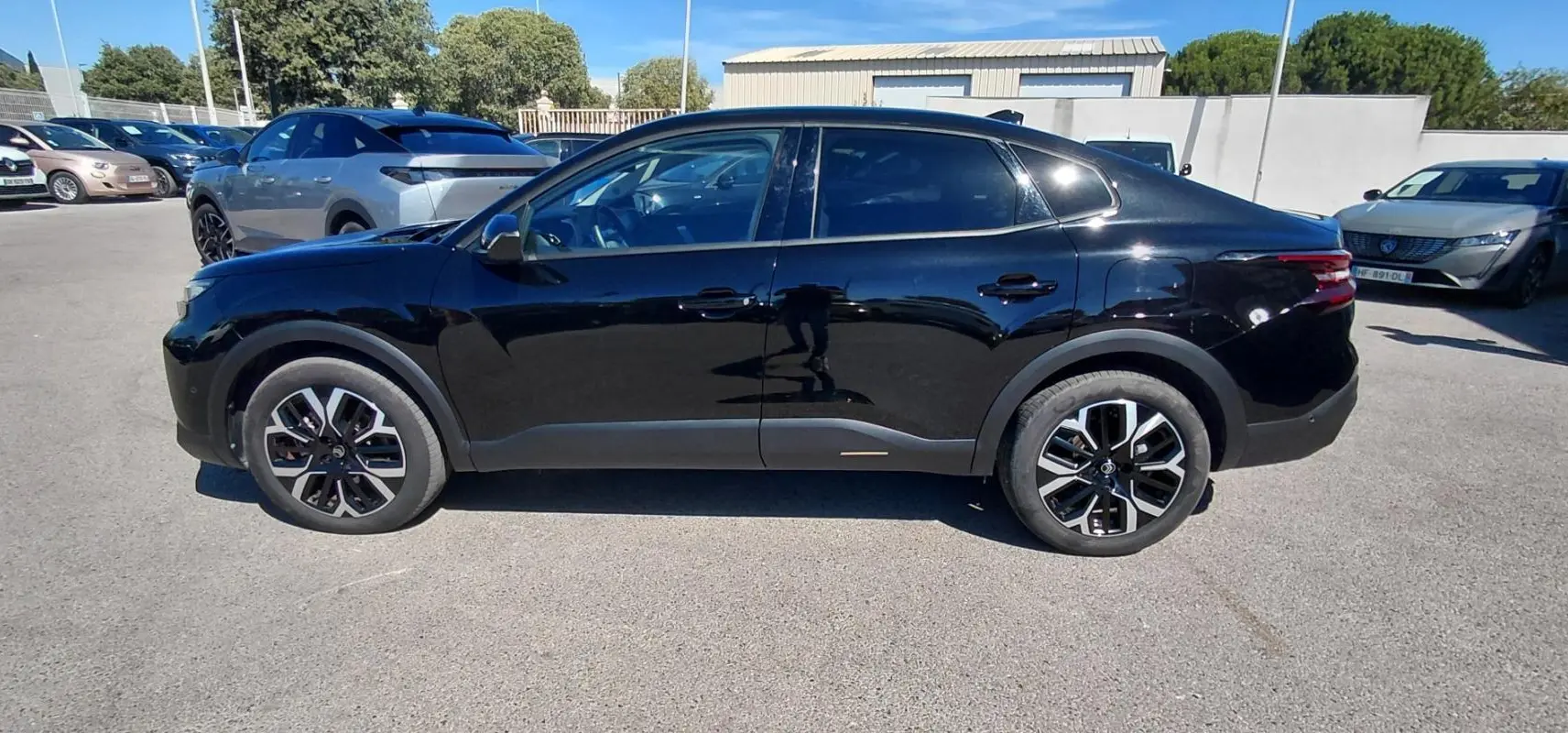 Profil côté gauche d'une Citroën C4 X hybride noire 2025 avec jantes alliage 17 pouces et toit ouvrant panoramique.