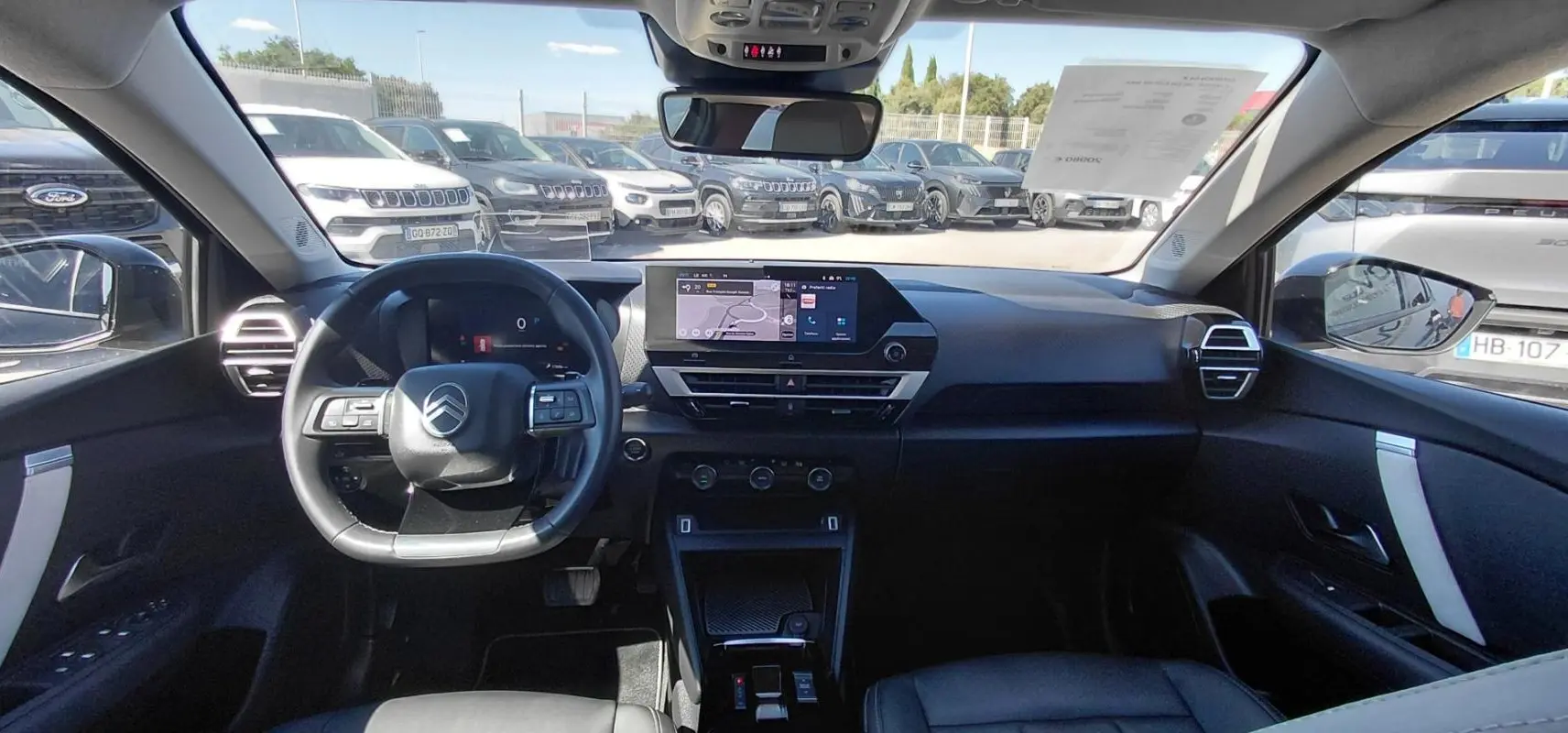 Vue intérieure avant du Citroën C4 X noir 2025, montrant le tableau de bord moderne et le volant cuir avec commandes intégrées.