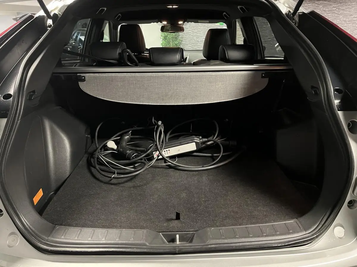 Coffre ouvert d'un Mitsubishi Eclipse Cross gris avec câble de recharge hybride visible et cache-bagages déployé.